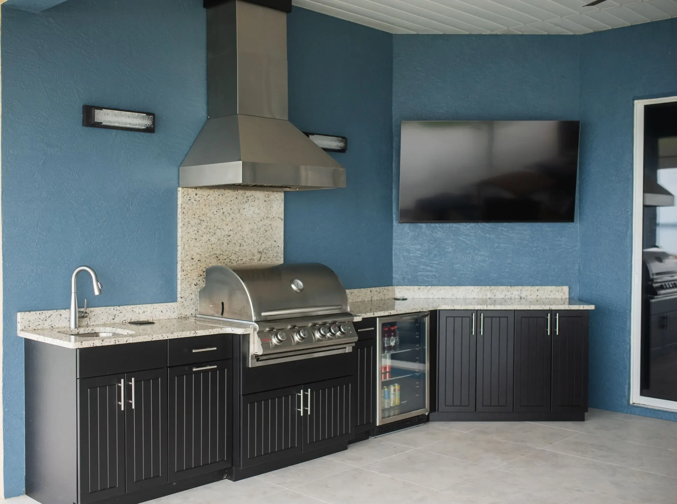 blue outdoor kitchen with sink, a grill and beverage refrigerator