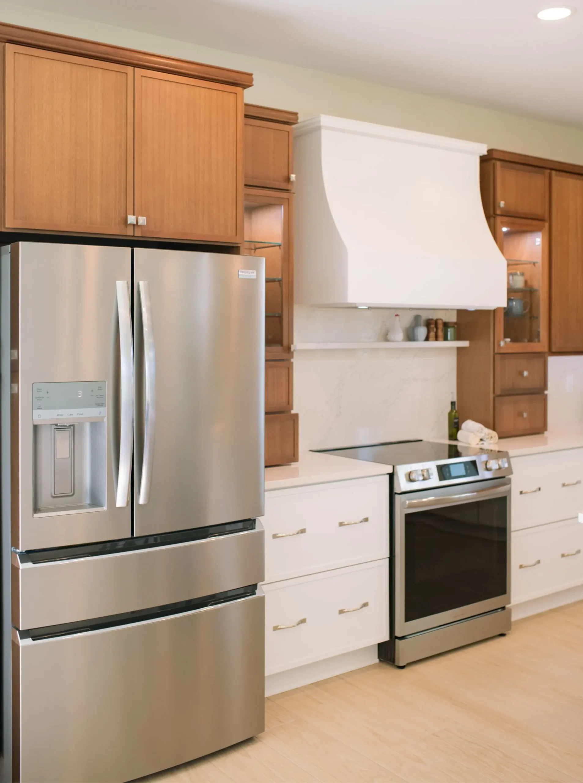 White range hood with a small ledge, countertop backsplash, and surrounding wood cabinetry