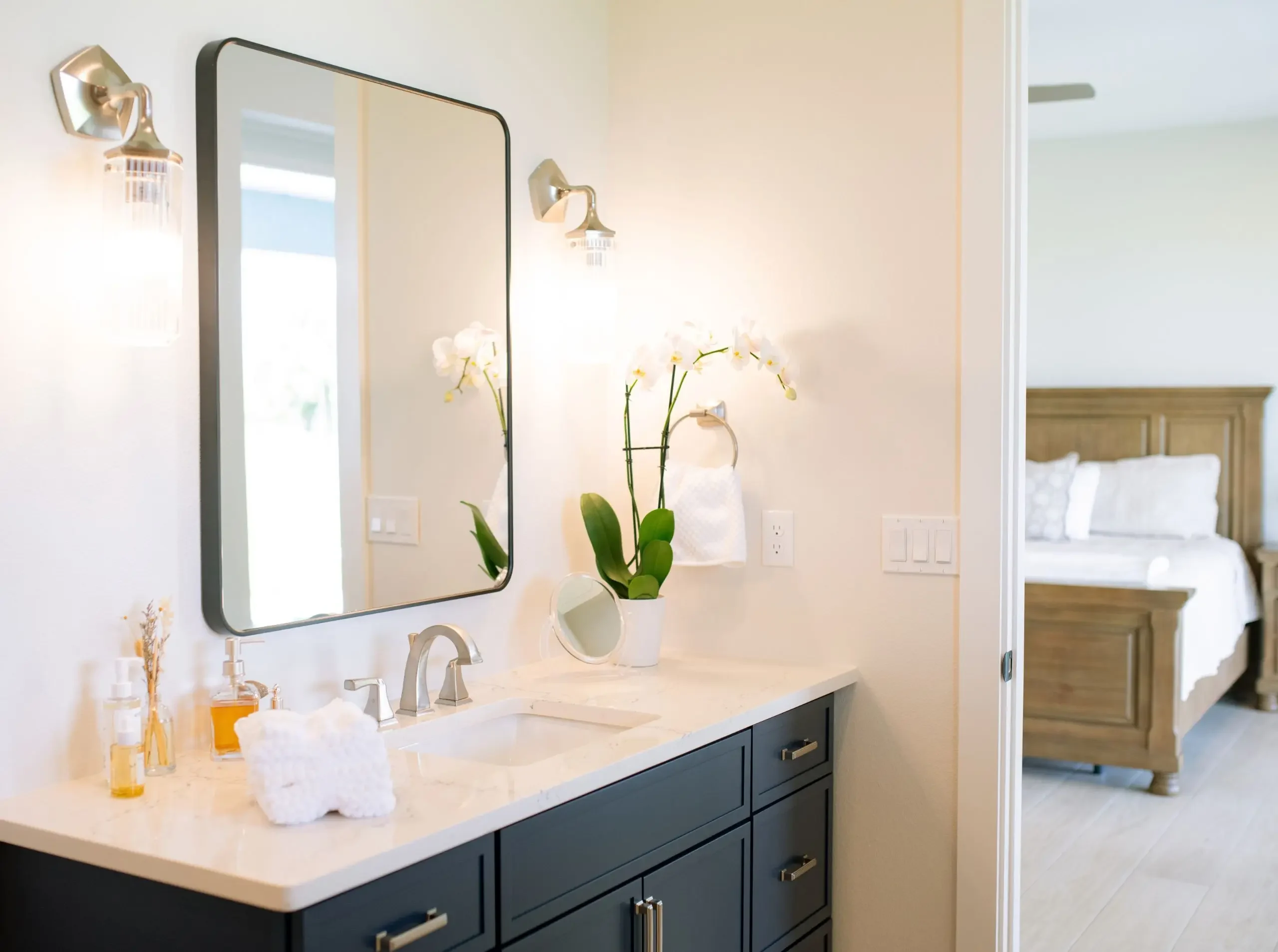 Primary bathroom with blue cabinetry, white countertop, and brass wall sconces