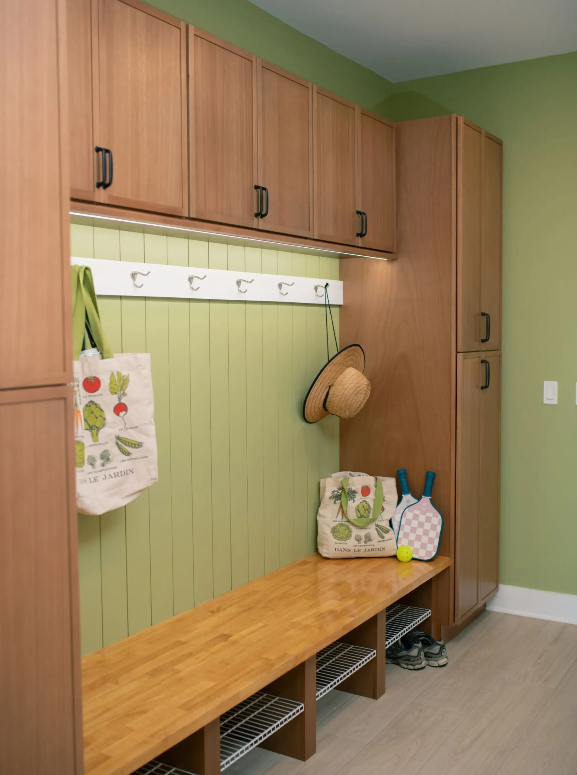 Custom mudroom with wood storage cabinets, built-in bench, coat hooks, and integrated lighting