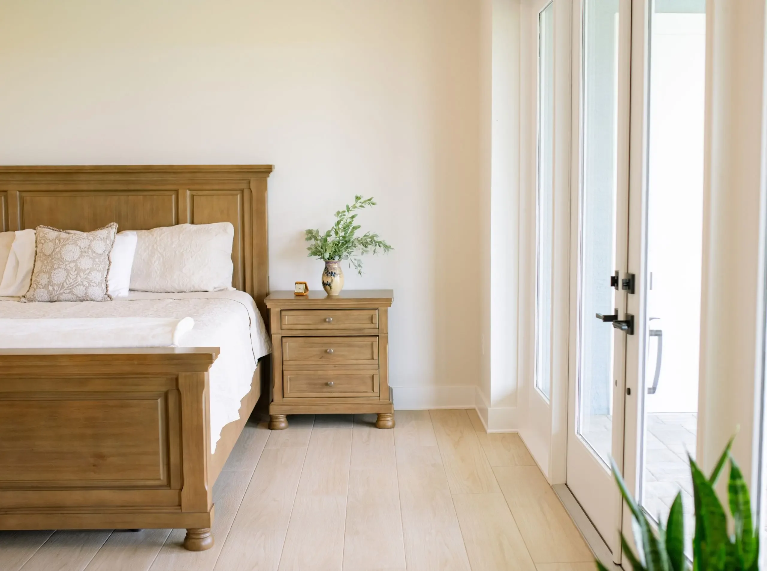 Light-filled primary bedroom with wood bedroom furniture and glass doors opening to the outdoors